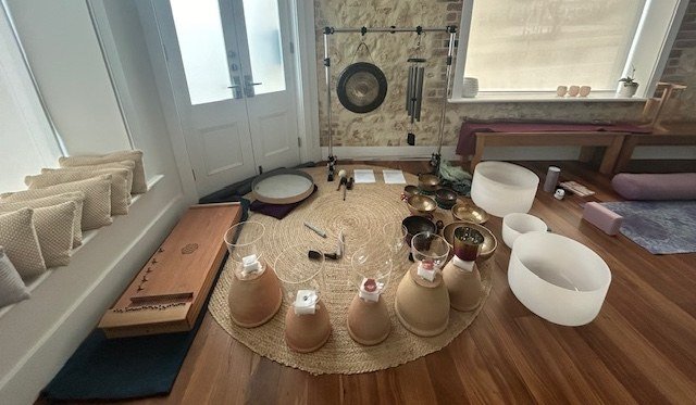 Monochord, crystal bowls, chalices and gongs arranged on a round woven rug.