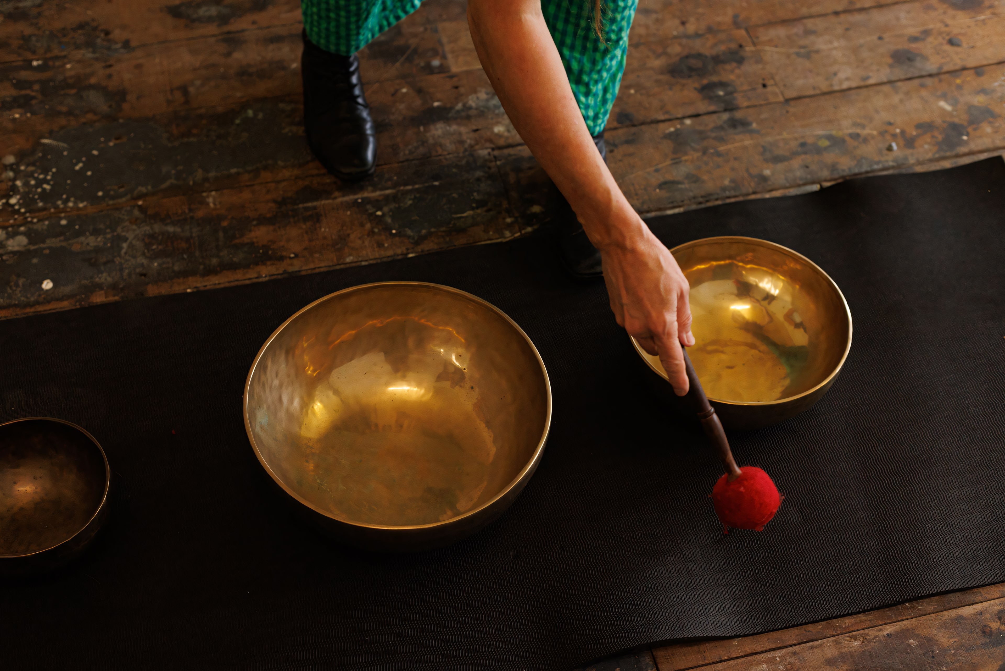 Danielle’s hand arranging brass singing bowls on a dark cloth.