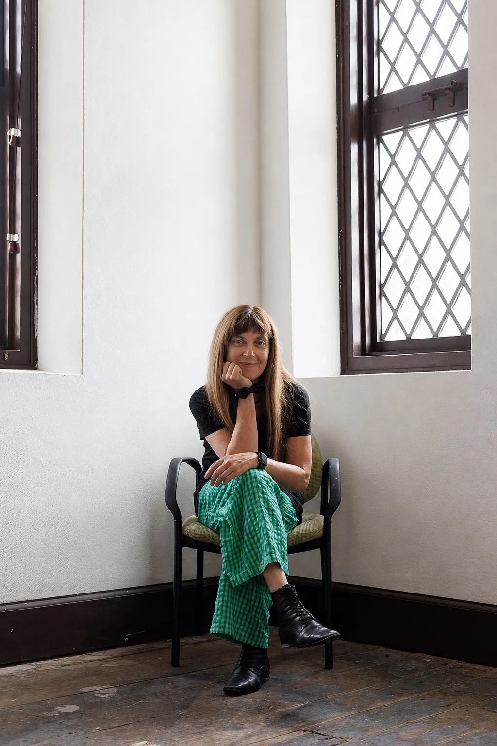 Danielle seated between tall windows in a quiet studio.