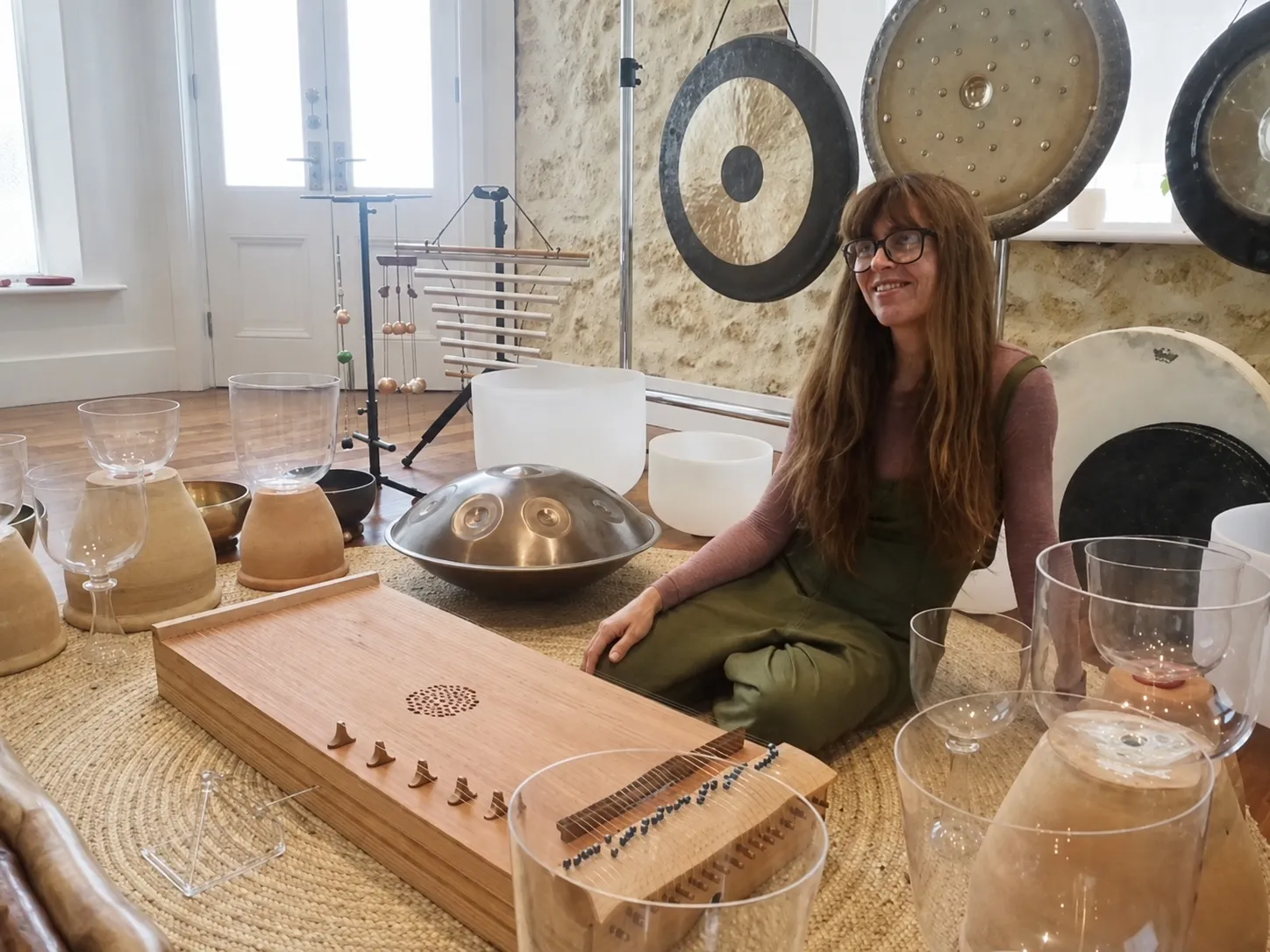 Danielle seated among gongs, crystal bowls and a monochord.