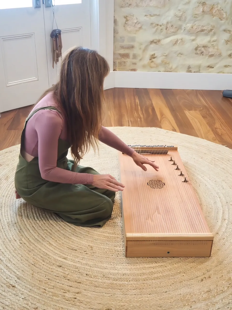 Danielle seated on the floor playing a wooden monochord.