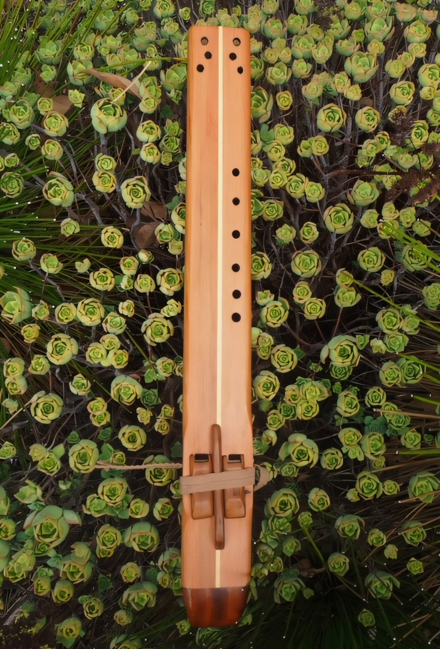 A wooden flute resting among green succulent flowers.