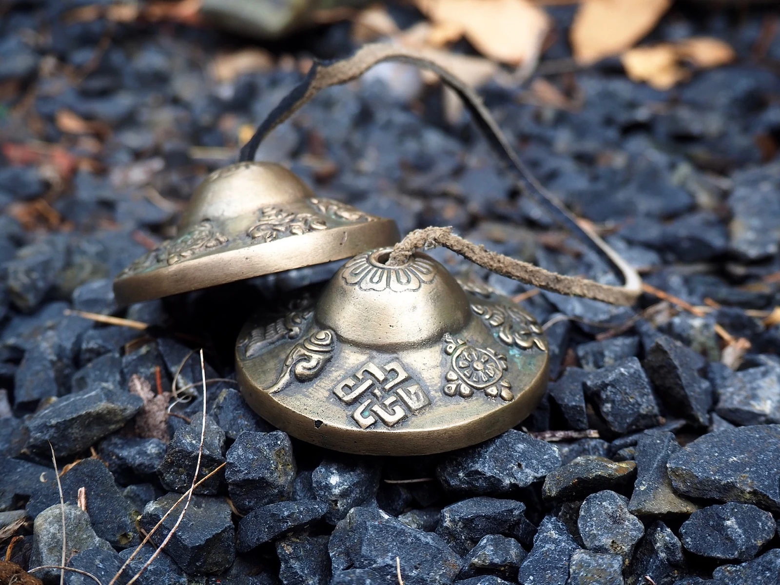 A pair of engraved brass tingsha resting on dark stones.