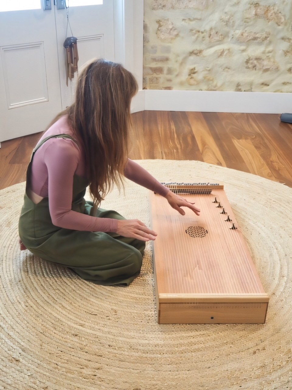 Danielle seated on a woven rug with her hands poised over a wooden monochord.