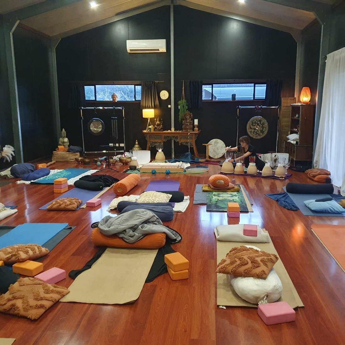 An open floor with mats, cushions and sound instruments beneath the studio rafters.