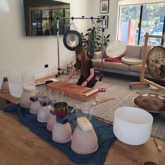 Danielle plays a monochord surrounded by crystal bowls and gongs in a light-filled room.