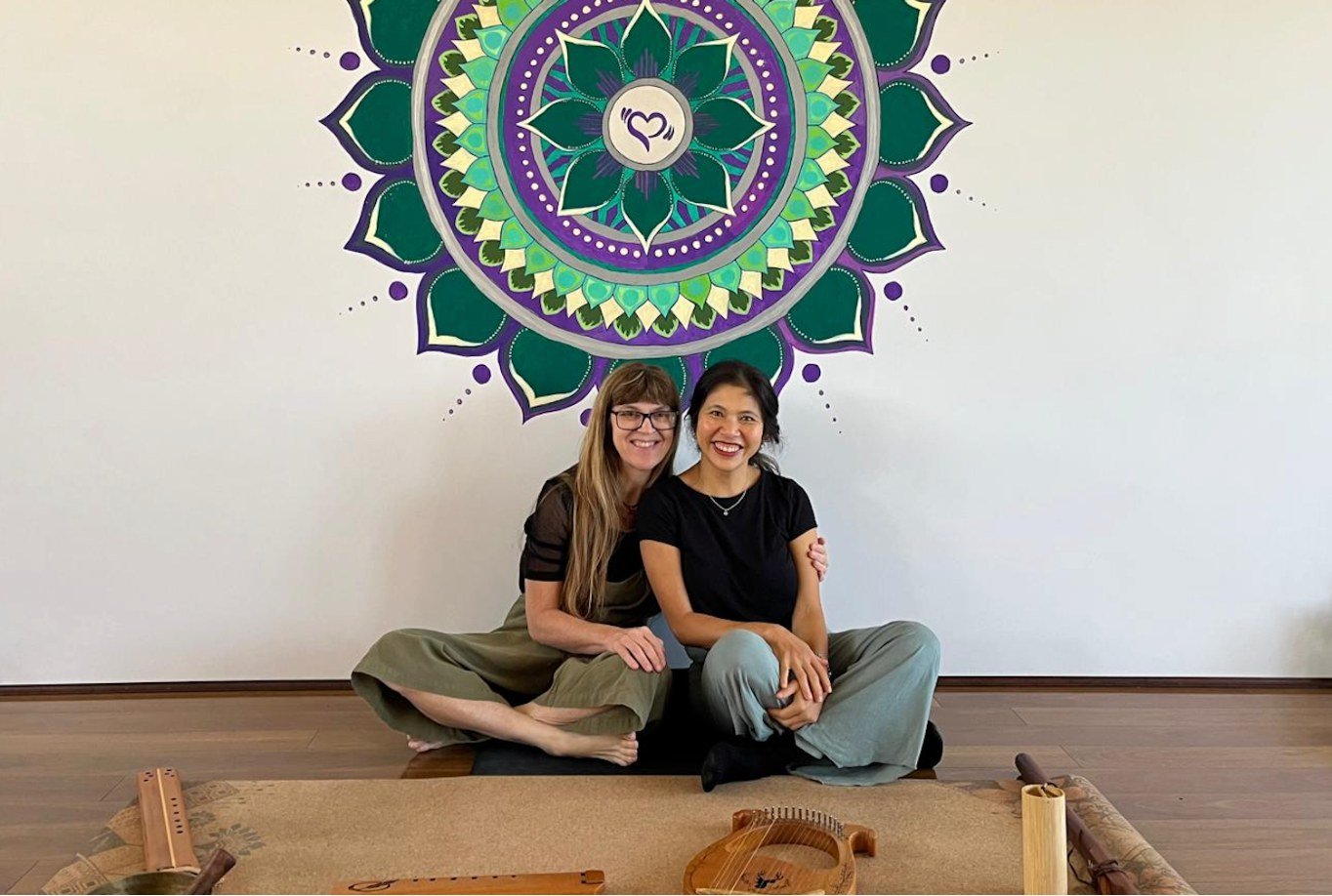 Danielle and Shanan sit together behind a monochord beneath a colourful mandala at Spanda.