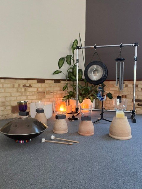 Gongs, crystal bowls and chimes arranged beside a brick wall at Tamara Yoga.