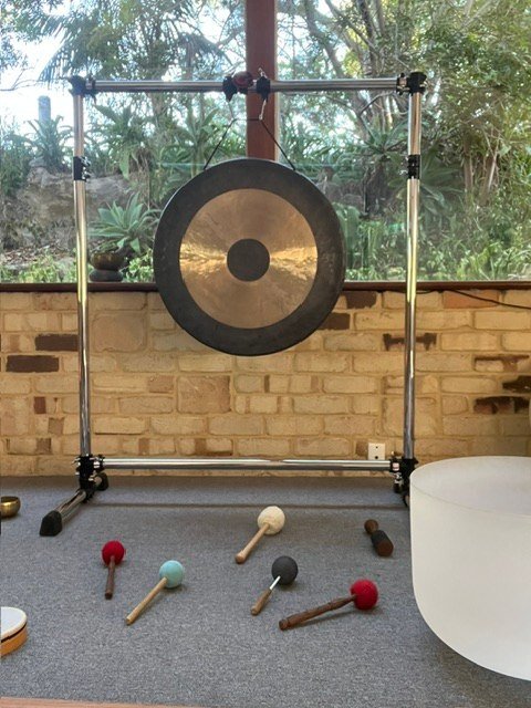 A suspended gong, coloured mallets and a white bowl beside the studio windows.